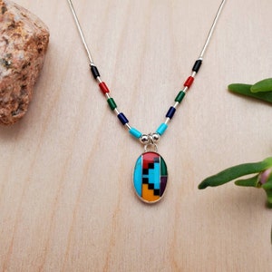 Puede incluir: Un collar de plata con un colgante ovalado multicolor. El colgante est&aacute; hecho de turquesa, rojo, naranja, verde, negro y blanco. El collar est&aacute; hecho de cuentas de plata y tiene una cadena de plata.