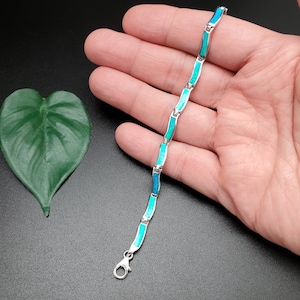 May include: A silver bracelet with blue and green opal inlay. The bracelet is made of small, linked pieces that form a wavy pattern.