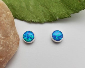 Könnte beinhalten: Ein Paar silberne Ohrstecker mit blauen Opal-Edelsteinen. Die Ohrringe sind rund und haben eine glatte, polierte Oberfläche.