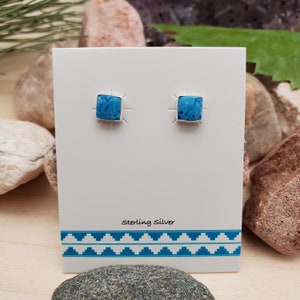 May include: A pair of sterling silver earrings with square turquoise stones. The earrings are displayed on a white card with the text "Sterling Silver".