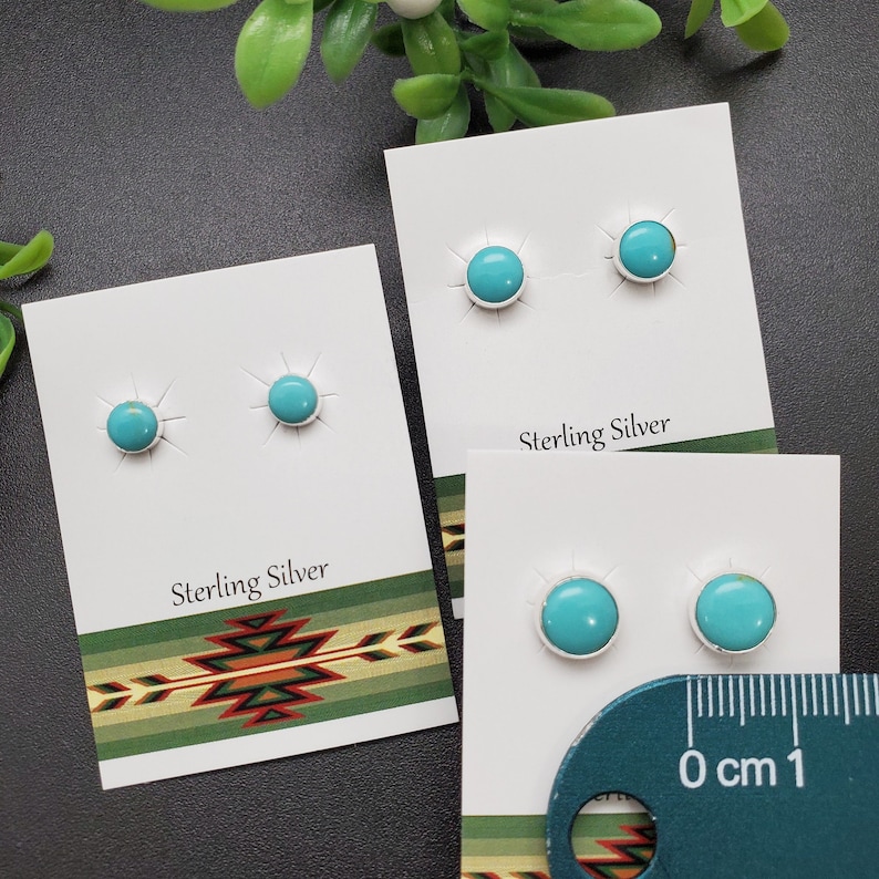 May include: Two pairs of turquoise stud earrings on white cards with the text "Sterling Silver". A ruler is in the bottom right corner of the image.