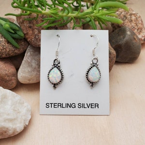 May include: A pair of sterling silver earrings with white opal teardrop stones. The earrings have a delicate, ornate design.