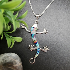 May include: A silver chain necklace with a multi-colored opal lizard pendant. The lizard is made of sterling silver and has a detailed design. The opal stones are set in the lizard's body and tail.