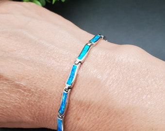 May include: A silver bracelet with blue opal stones. The bracelet is made of small, rectangular links that are connected together. The opal stones are set in the links and are a light blue color.