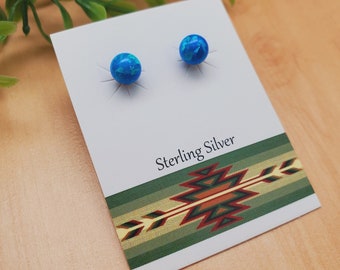 May include: A pair of blue opal stud earrings on a white card with the text "Sterling Silver" and a green, brown, and gold patterned design.