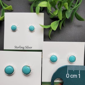 May include: Two pairs of turquoise stud earrings on white cards. The earrings are set in sterling silver. The cards have the words "Sterling Silver" printed on them. A ruler is in the bottom right corner of the image.