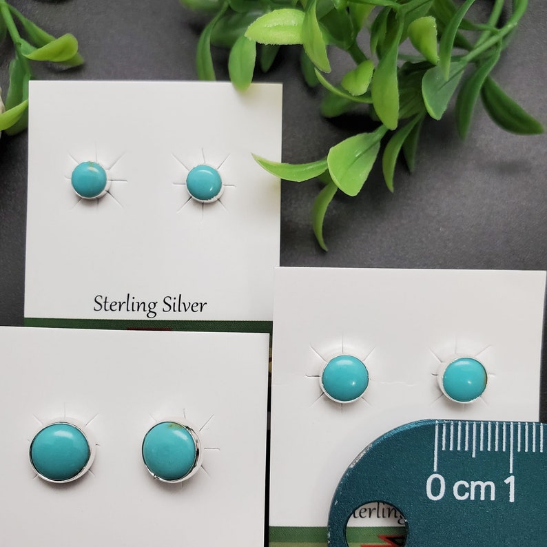 May include: Two pairs of turquoise stud earrings on white cards. The earrings are set in sterling silver. The cards have the words "Sterling Silver" printed on them. A ruler is in the bottom right corner of the image.