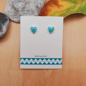 May include: A pair of sterling silver heart-shaped earrings with turquoise stones. The earrings are on a white card with the text "Sterling Silver" printed on it.
