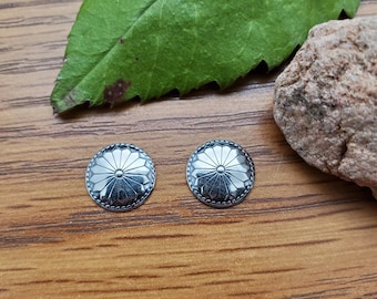 May include: Two silver-toned earrings with a floral design. The earrings are round and have a raised, textured pattern.