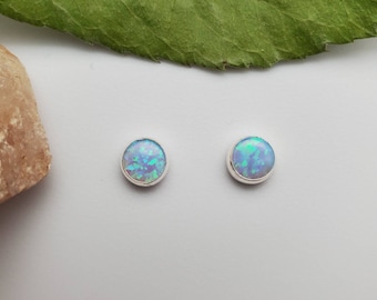Könnte beinhalten: Ein Paar silberne Ohrstecker mit runden blauen Opal-Steinen.