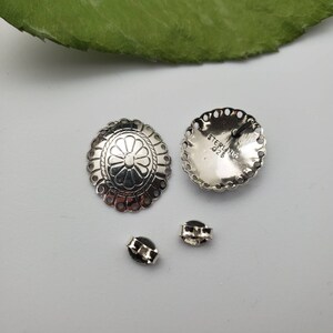 May include: A pair of silver earrings with a floral design. The earrings are marked "STERLING 925" on the back.