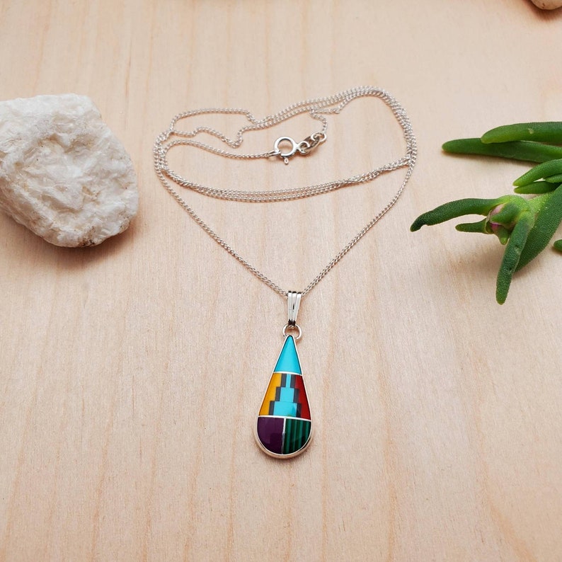 Puede incluir: Un collar de cadena de plata con un colgante en forma de l&aacute;grima. El colgante est&aacute; hecho de plata e incrustado con piedras turquesa, rojas, amarillas, verdes y moradas.