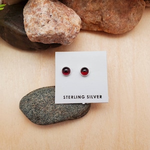 May include: A pair of sterling silver stud earrings with red gemstone accents. The earrings are displayed on a white card with the text "STERLING SILVER".