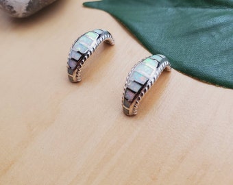 May include: A pair of silver hoop earrings with a white opal inlay. The earrings are curved and have a textured edge.