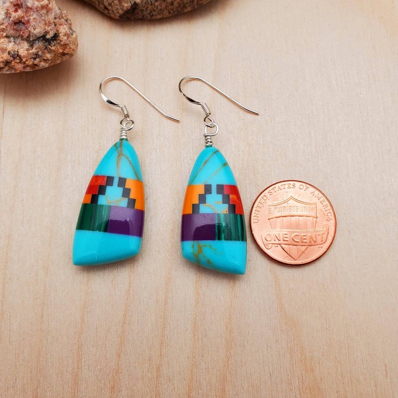May include: A pair of turquoise and multi-colored inlay dangle earrings with silver ear wires. The earrings are about the size of a US penny.