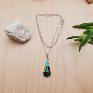 Puede incluir: Un collar de cadena de plata con un colgante en forma de l&aacute;grima. El colgante est&aacute; hecho de plata e incrustado con piedras turquesa, moradas, amarillas, rojas y verdes.