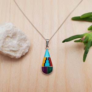 Puede incluir: Un collar de cadena de plata con un colgante en forma de l&aacute;grima. El colgante est&aacute; hecho de turquesa, rojo, amarillo, verde y morado.