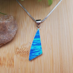 May include: A silver chain necklace with a pendant featuring a blue and green opal gemstone. The pendant is shaped like a triangle with rounded edges.