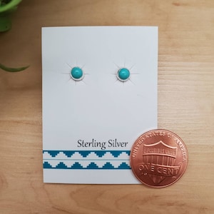 Può includere: Un paio di orecchini in argento sterling con pietre turchesi. Gli orecchini sono esposti su una carta bianca con le parole "Sterling Silver" stampate su di essa. Un centesimo è incluso come riferimento per le dimensioni.