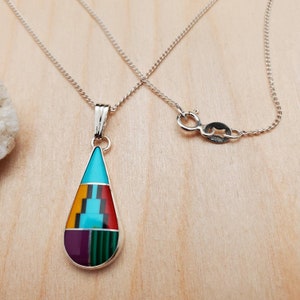 Puede incluir: Un collar de cadena de plata con un colgante en forma de l&aacute;grima. El colgante est&aacute; hecho de turquesa, rojo, amarillo, verde y morado.