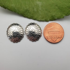 May include: Two silver-toned metal embellishments with a floral design. The embellishments are about the size of a US penny.