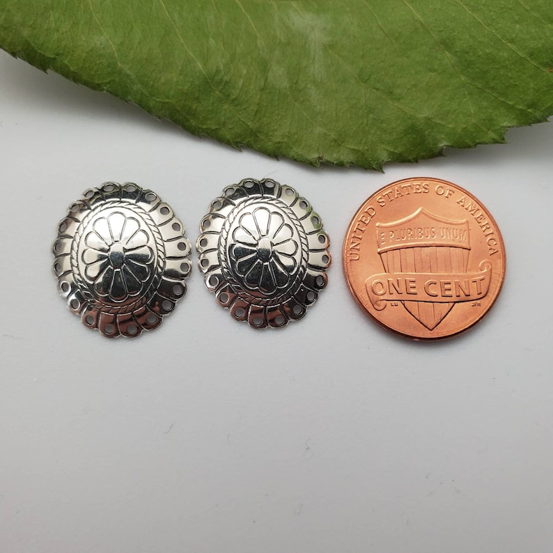 May include: Two silver-toned metal embellishments with a floral design. The embellishments are about the size of a US penny.