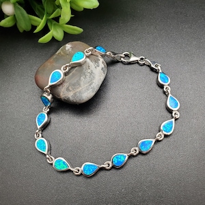 Puede incluir: Un brazalete de plata con piedras de ópalo azul en forma de lágrima. El brazalete tiene un cierre de langosta.