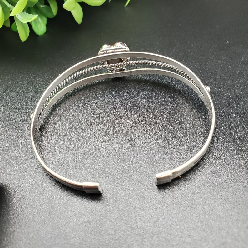 Op de afbeelding: Zilveren armband met een decoratieve, veelkleurige steen in het midden.