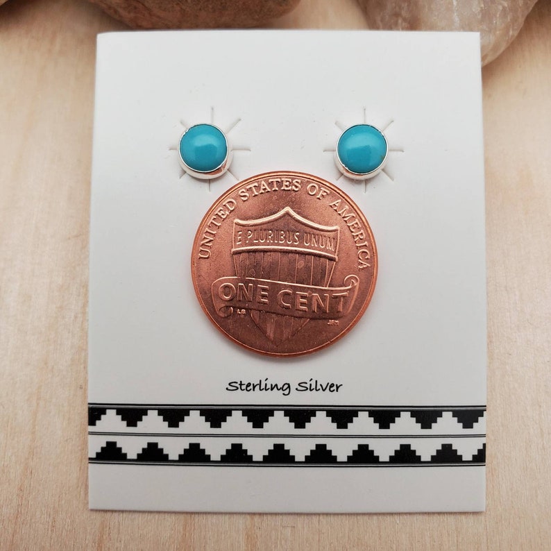 May include: A pair of sterling silver earrings with turquoise stones. The earrings are shown next to a US penny for size comparison. "Sterling Silver" is printed on the card.