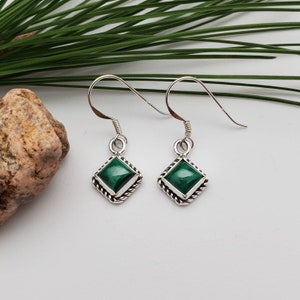May include: A pair of silver earrings with green malachite stones set in a square shape with a rope-like border.
