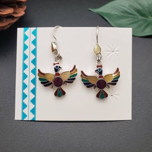 May include: A pair of silver dangle earrings with a colorful bird design. The birds are made of silver and have a yellow, red, green, blue, and purple enamel finish. The earrings are hanging from a silver hook.