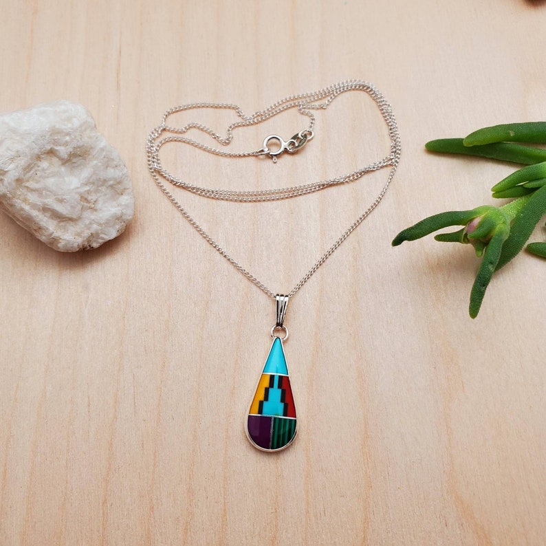 Puede incluir: Un collar de cadena de plata con un colgante en forma de l&aacute;grima. El colgante est&aacute; hecho de turquesa, rojo, amarillo, verde y piedras moradas.