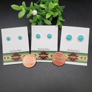 May include: Three pairs of turquoise earrings on white cards with the text "Sterling Silver". The cards are on a black surface with a penny below each card.
