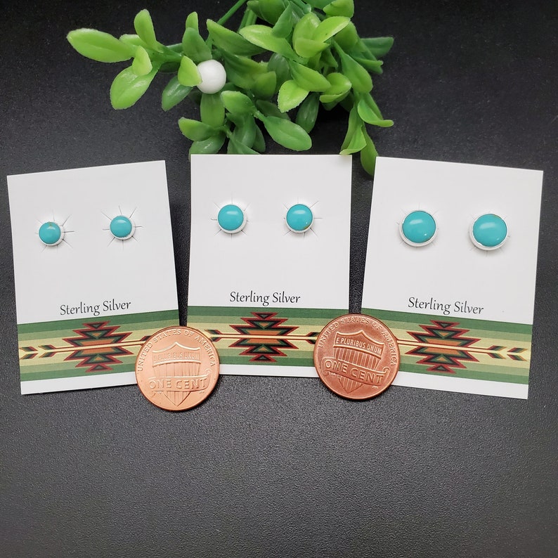 May include: Three pairs of turquoise earrings on white cards with the text "Sterling Silver". The cards are on a black surface with a penny below each card.