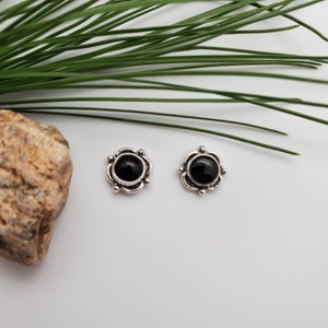 May include: A pair of silver earrings with black gemstone accents. The earrings are round and have a delicate floral design.