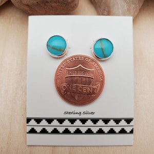 May include: A pair of sterling silver earrings with turquoise stones. The earrings are displayed on a white card with a penny for size comparison. The card also says "Sterling Silver".