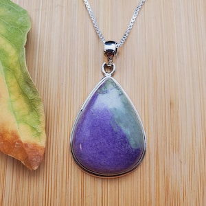 Könnte beinhalten: Eine silberne Halskette mit einem tropfenförmigen Anhänger aus violettem und grünem Edelstein.