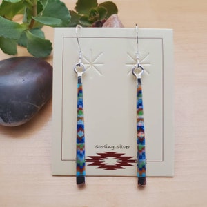 May include: Sterling silver dangle earrings with a geometric pattern of turquoise, red, green, and brown stones. The earrings are displayed on a card with the text "Sterling Silver".