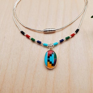 Puede incluir: Un collar de cadena de plata con un colgante ovalado multicolor. El colgante est&aacute; hecho de turquesa, rojo, verde, negro y amarillo. El collar tiene un cierre magn&eacute;tico.