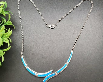 May include: A silver necklace with a blue opal pendant in the shape of a curved line. The pendant is made of small, blue opal stones set in silver.