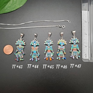 May include: Five silver pendants with colorful inlay designs. The pendants feature a stylized human figure with geometric patterns and turquoise, coral, and other stones. The pendants are labeled with numbers 43 through 47.