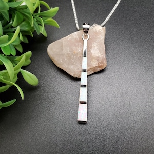 May include: A silver necklace with a long, white opal pendant. The pendant is made of multiple opal pieces set in silver.