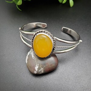 May include: A silver bangle bracelet with a yellow oval gemstone set in a silver bezel. The bracelet has a braided design.
