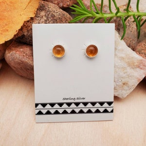 May include: A pair of sterling silver earrings with amber stones. The earrings are on a white card with the words "Sterling Silver" printed on it.
