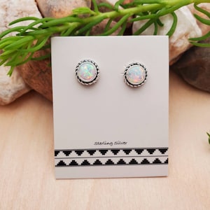 May include: A pair of sterling silver earrings with white opal stones set in a rope design. The earrings are displayed on a white card with the words "Sterling Silver" printed on it.