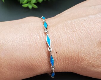 May include: A silver bracelet with a row of blue opal stones in a diamond shape.