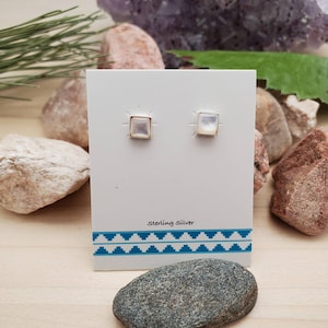 May include: A pair of sterling silver earrings with square shaped white mother of pearl stones. The earrings are displayed on a white card with the text "Sterling Silver" printed on it.