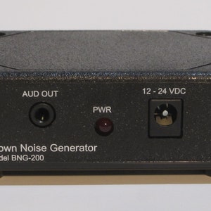 May include: Black box-shaped brown noise generator with a power indicator light, an audio output jack, and a power input jack. The text on the front reads "Brown Noise Generator Model BNG-200" and "12 - 24 VDC".