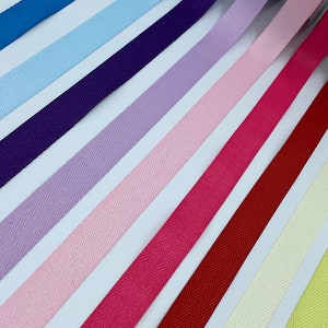 Op de afbeelding: Assortiment van 10 verschillende kleuren herringbone lint. De kleuren zijn: marineblauw, koninklijkblauw, lichtblauw, paars, lavendel, roze, felroze, bordeauxrood, crème en geel.