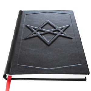 Puede incluir: Un libro encuadernado en cuero negro con un marcap&aacute;ginas de cinta roja. La portada presenta un dise&ntilde;o geom&eacute;trico en relieve.